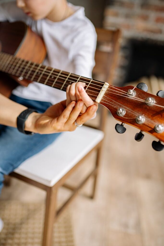 Close-up of a child learning guitar with adult guidance, focused on hands and instrument.
