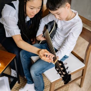 A child receiving guitar lessons from a music teacher, focusing on technique and chords.